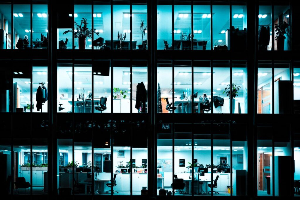 Night view of an illuminated modern office building showcasing workspaces through large windows.